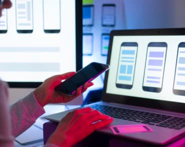 person looking at a phone in front of a laptop